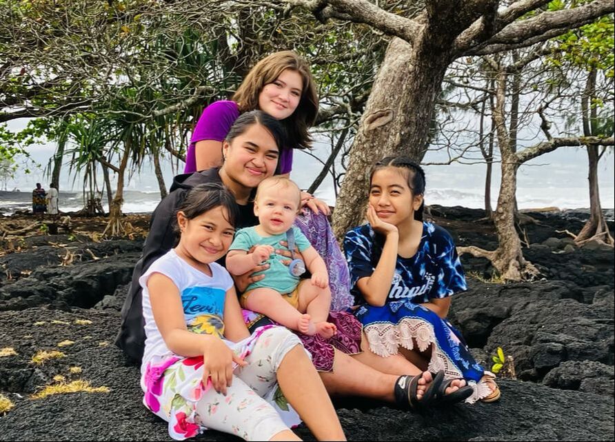 Polynesian children sitting under the trees by the ocean in Hawaii